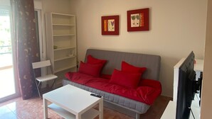 Un salon avec un canapé gris, des coussins rouges, une table basse blanche et un meuble TV blanc.
