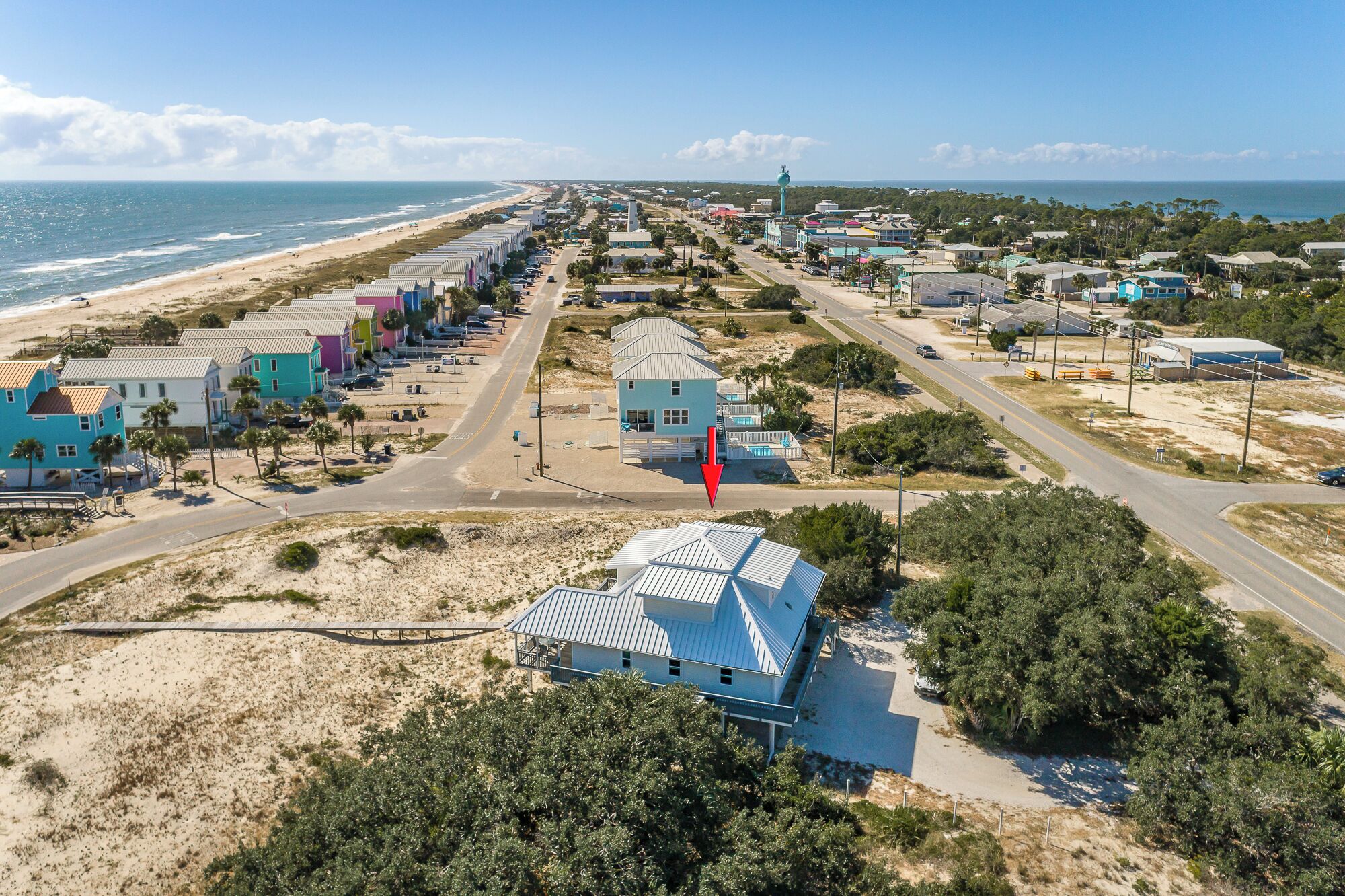 Un pueblo costero con propiedades frente a la playa, una torre de agua destacada y una carretera despejada que lleva a la playa.
