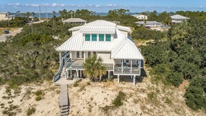 A beachfront house with a large deck, a staircase leading to the main entrance, and a view of the ocean.