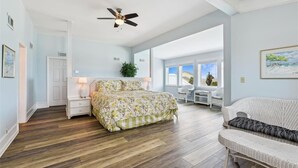 A bedroom with a bed, nightstands, a ceiling fan, and a view of the outdoors.