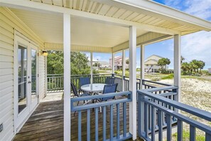 Une terrasse extérieure couverte, dotée d’une table et de chaises, qui offre une vue sur une plage et d’autres bâtiments.