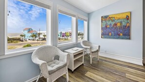 A room with large windows, wicker chairs, a small table, and a colorful painting on the wall.