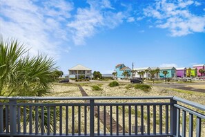 A beachside property with a wooden deck, a sandy beach, and colorful houses in the background.
