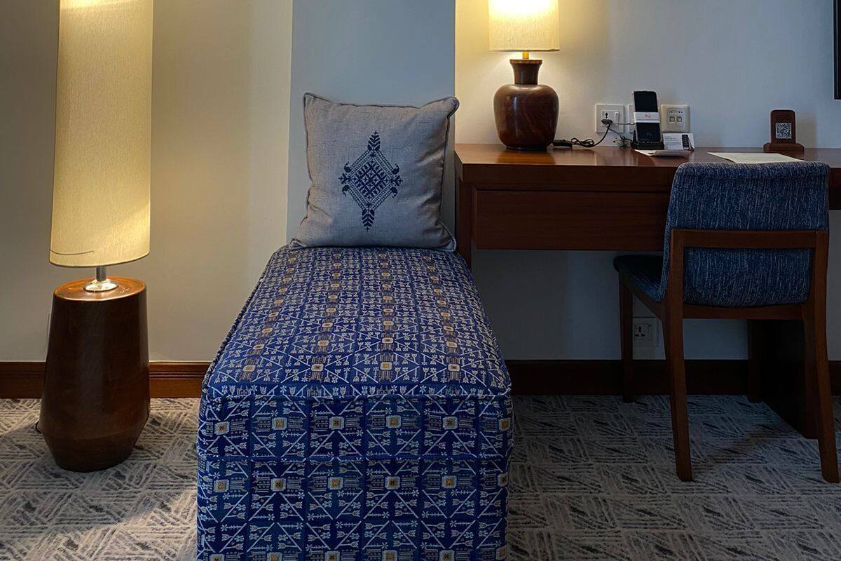 A hotel room with a bed, a desk with a lamp, a chair, and a small table with a phone and charger.