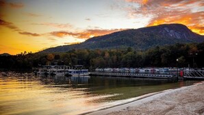 A waterfront dock with boats, a sandy beach, and a forested hill in the background. - Quail cove 1616 at Rumbling Bald (Lake Lure)