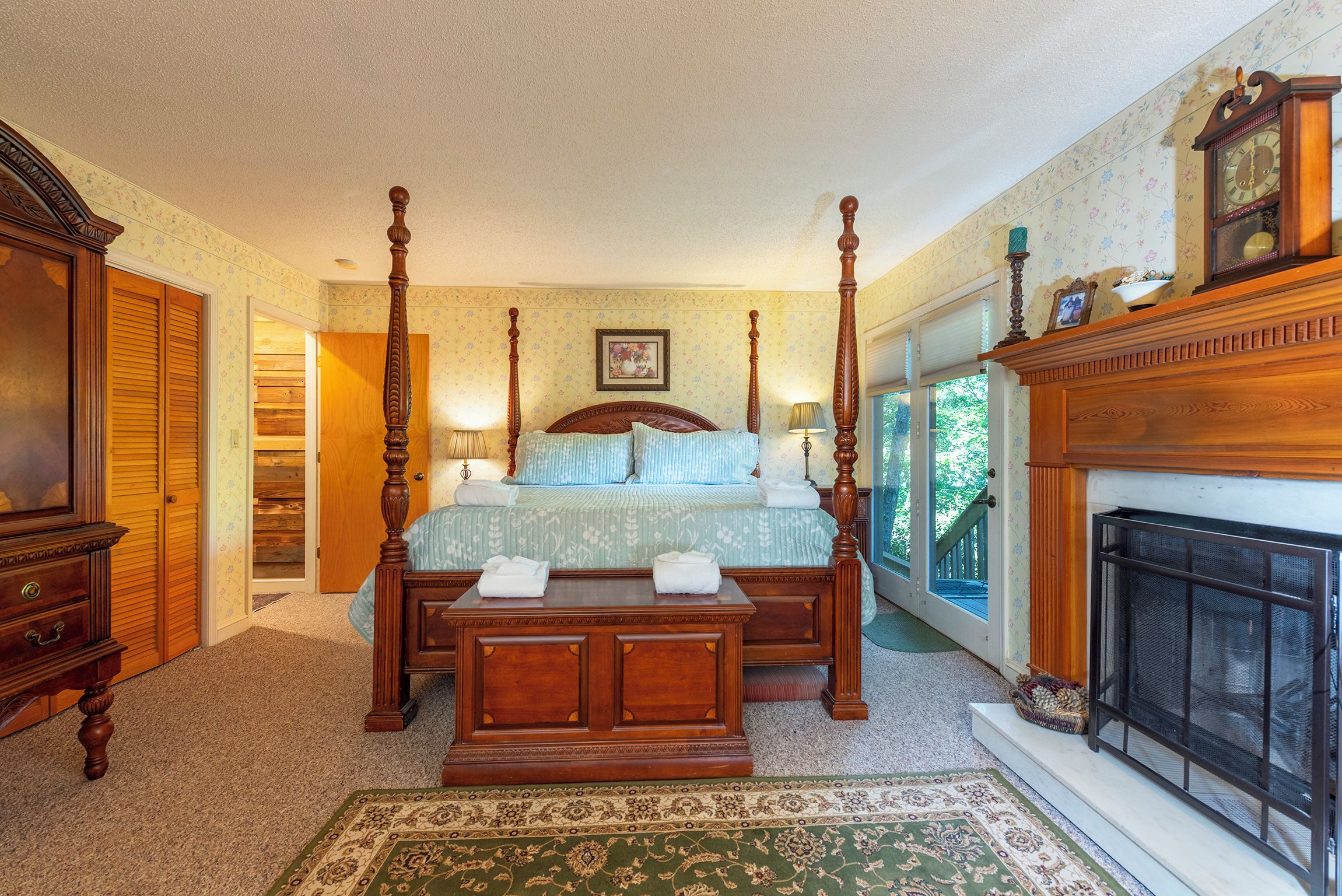 A traditional bedroom with a four-poster bed, a fireplace, and a view of the outdoors.