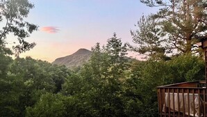 A forested area with a wooden deck and a mountain in the background. - Quail cove 1616 at Rumbling Bald (Lake Lure)
