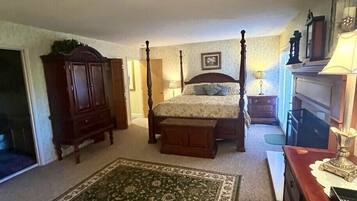A bedroom with a four-poster bed, a wooden dresser, a nightstand, a lamp, and a large area rug.