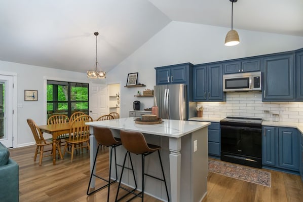 A modern kitchen with blue cabinets, a white island, and a black stove. - Turkey Run at Rumbling Bald (Lake Lure)
