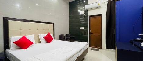 A hotel room with a large bed, two red pillows, a dark green accent wall, a wooden door, and a blue curtain.