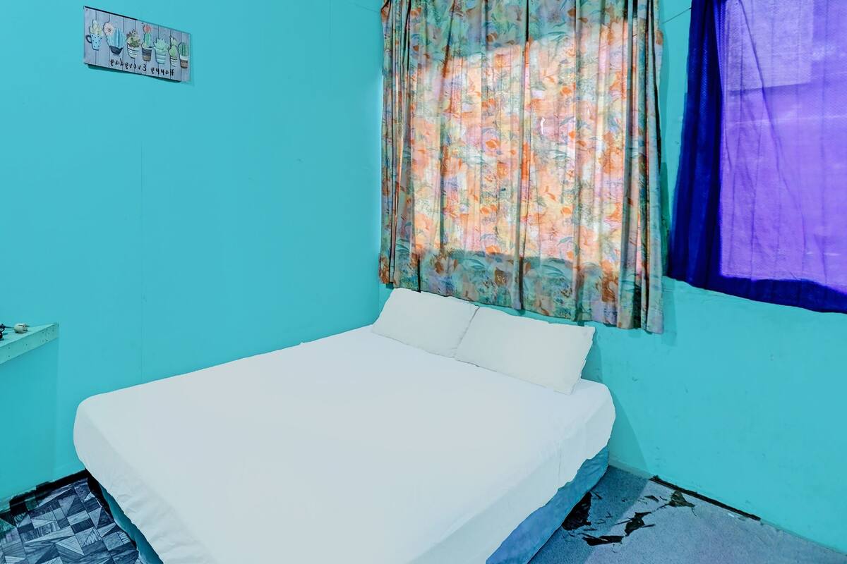 A small, single-bed room with a plain white bedspread, a floral curtain, and a blue wall.