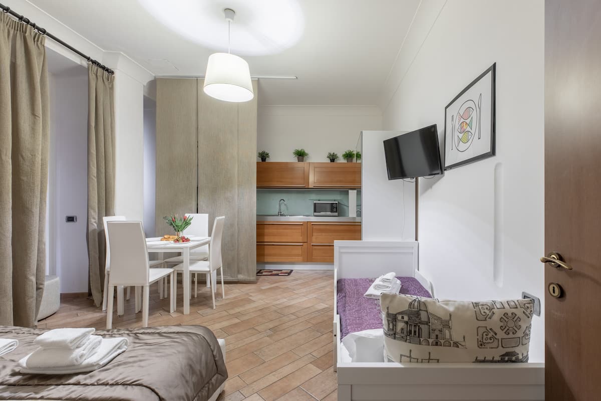 Kompakti hotellihuone, jossa on sänky, pieni ruokapöytä, sohva, televisio ja pieni keittiönurkkaus.