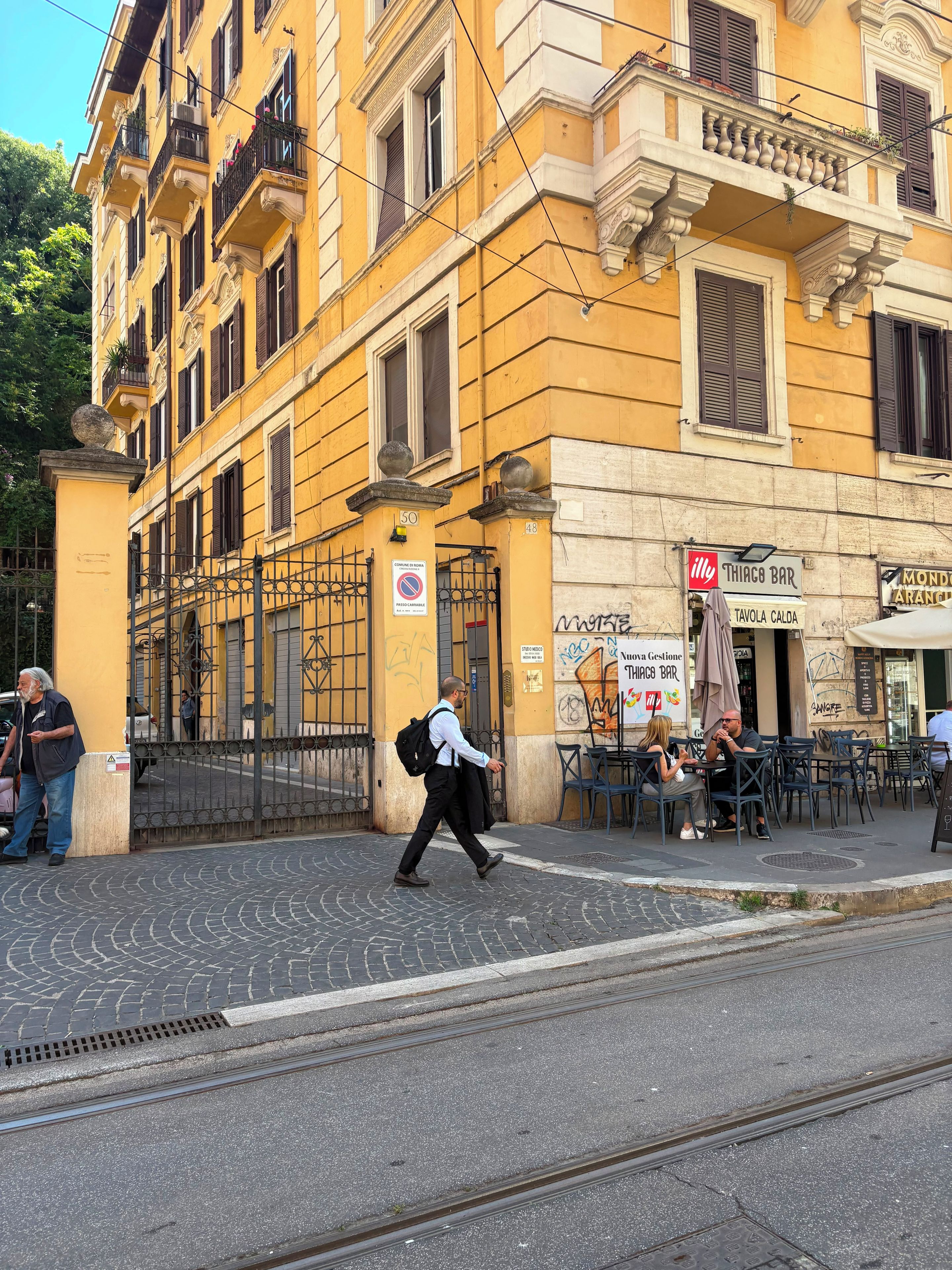 Une rue avec un immeuble jaune, un bar et des tables à l’extérieur.