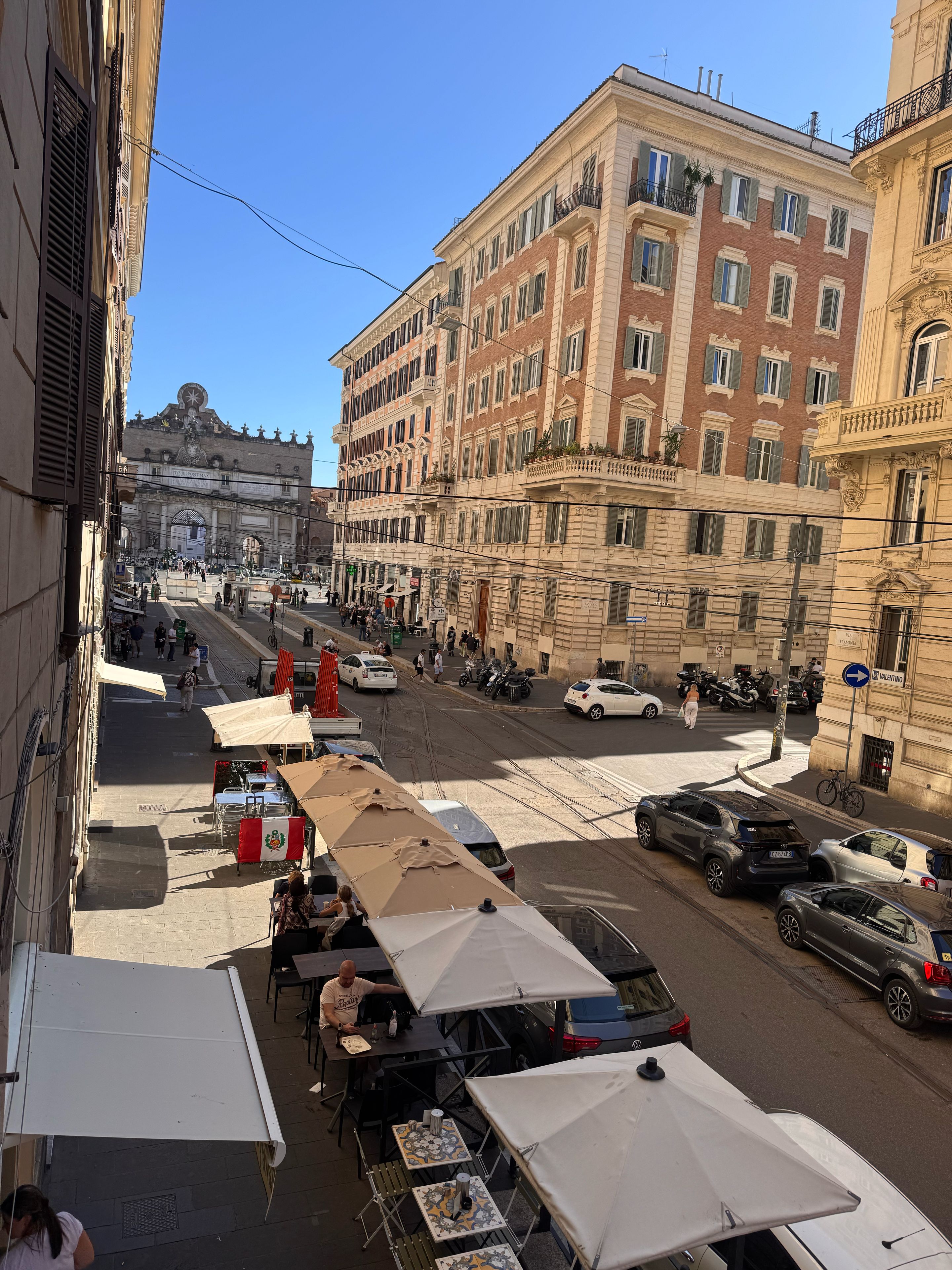 Une vue de rue avec des terrasses, des voitures garées et des bâtiments historiques.