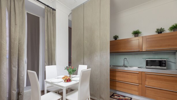 A compact kitchen with wooden cabinets, a microwave, and a dining area with a white table and chairs. - Flaminiarooms (Rome)