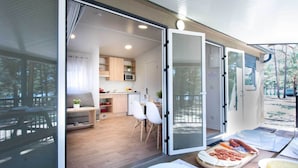 A modern kitchen with wooden cabinets, a microwave, and a dining area with white chairs. - Camping Urbión (Soria)