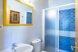 A bathroom with a white sink, a toilet, and a shower with blue-tiled walls. - Camping Urbión (Soria)