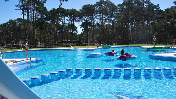 A swimming pool with a water slide, surrounded by trees. - Camping Urbión (Soria)