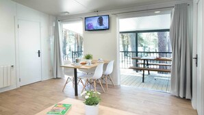 A modern room with a wooden table, chairs, a TV, and a balcony with a wooden deck. - Camping Urbión (Soria)