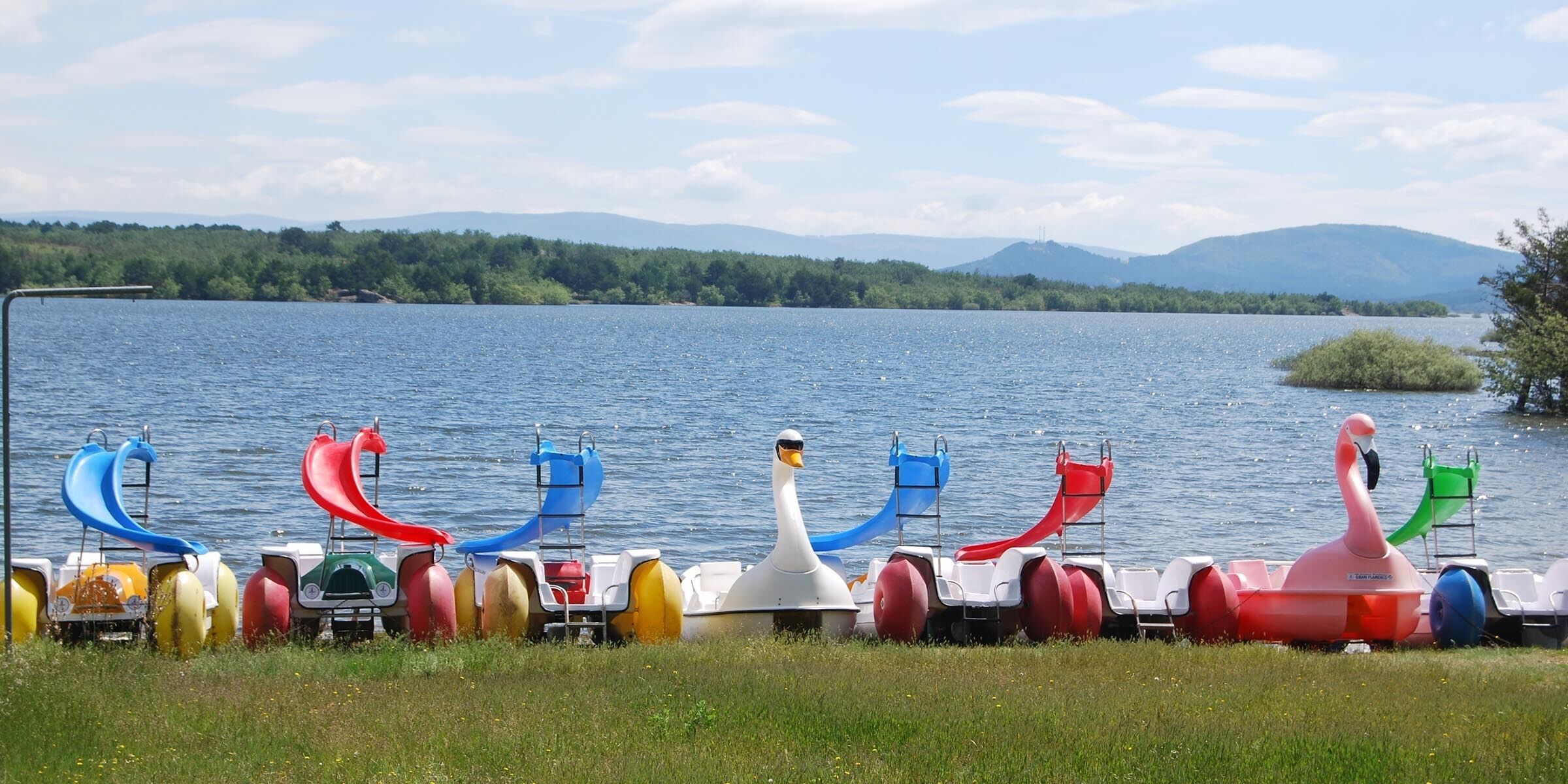 A row of colorful watercraft by a lake with mountains in the background.