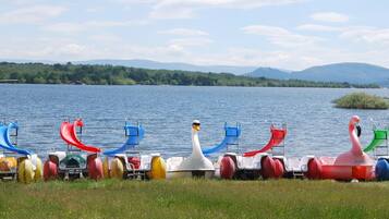A row of colorful watercraft by a lake with mountains in the background.