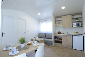 A compact kitchen with a microwave, sink, and wooden cabinets. There is a dining table with chairs and a small plant on the table. - Camping Urbión (Soria)