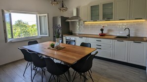 Ett modernt kök med vita skåp, ett matbord i trä, svarta stolar och hängande lampor.