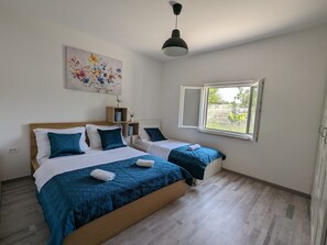Une chambre avec deux lits, une fenêtre, un luminaire au plafond et un tableau représentant des motifs floraux.
