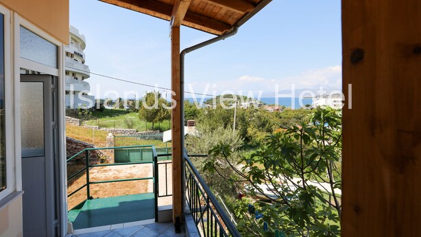 A balcony with a wooden ceiling, a view of a building in the background, and a green outdoor area. - Islands View Hotel (Ksamil)