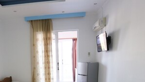 A narrow hallway with a door leading to a bright room, a small refrigerator, and a wall-mounted TV. - Islands View Hotel (Ksamil)