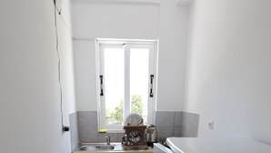A small, bright kitchen with a window, a sink, and a dish rack. - Islands View Hotel (Ksamil)