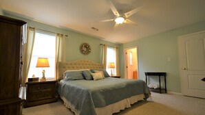A bedroom with a bed, a nightstand, a dresser, a ceiling fan, and a door.