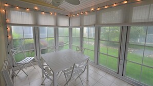 A sunroom with a table and chairs, large windows, and string lights.
