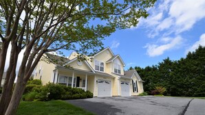 A two-story house with a garage, surrounded by greenery and a clear sky.