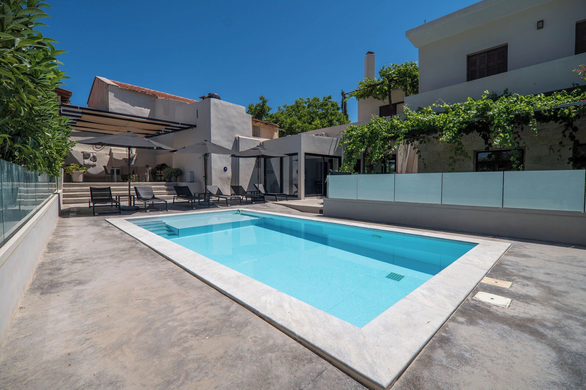 Une piscine rectangulaire, agrémentée de chaises longues et de parasols, entourée de bâtiments modernes et de verdure.