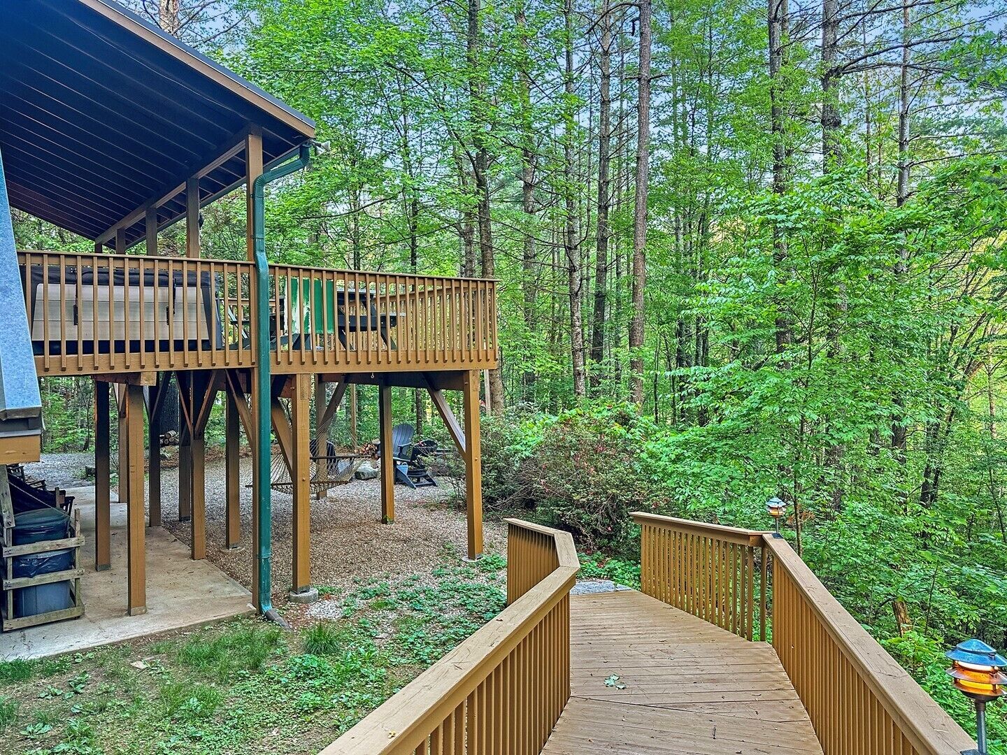 Une terrasse en bois mène à un chalet doté d’un toit en métal, le tout étant entouré d’une forêt dense.