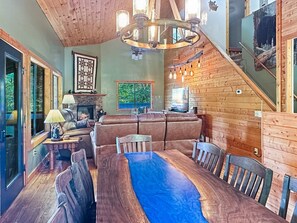 A cozy interior with a fireplace, leather sofa, dining table, and a view of the outdoors. - Bear's Den - Nantahala Gorge seclusion and convenience + free rafting (Bryson City)