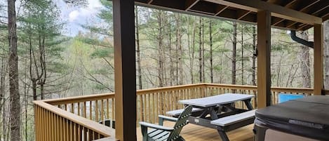 A covered deck with picnic tables and benches, surrounded by trees.