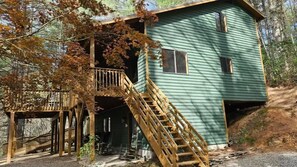 A wooden cabin with a wooden staircase leading to a deck, surrounded by trees.