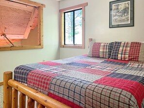 A bedroom with a bed, a window, a framed picture on the wall, and a wooden headboard.