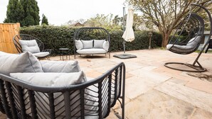 Un patio con mobiliario de mimbre, incluyendo una silla y un sofá, y una mecedora colgante.