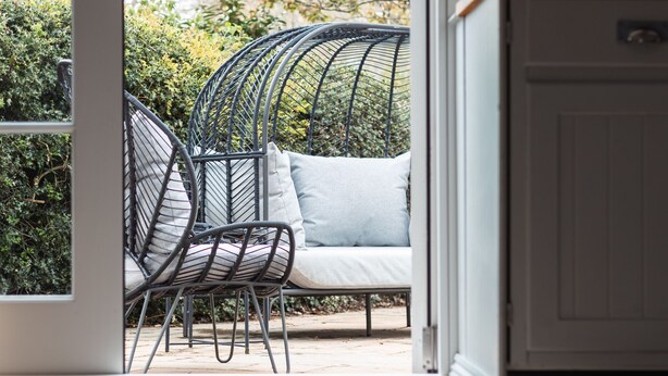 Puerta abierta que da a un patio con una silla de mimbre y cojines.
