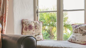 Un siège de fenêtre agrémenté de coussins à motifs floraux, une vue sur la verdure à l’extérieur et une porte avec un interrupteur.