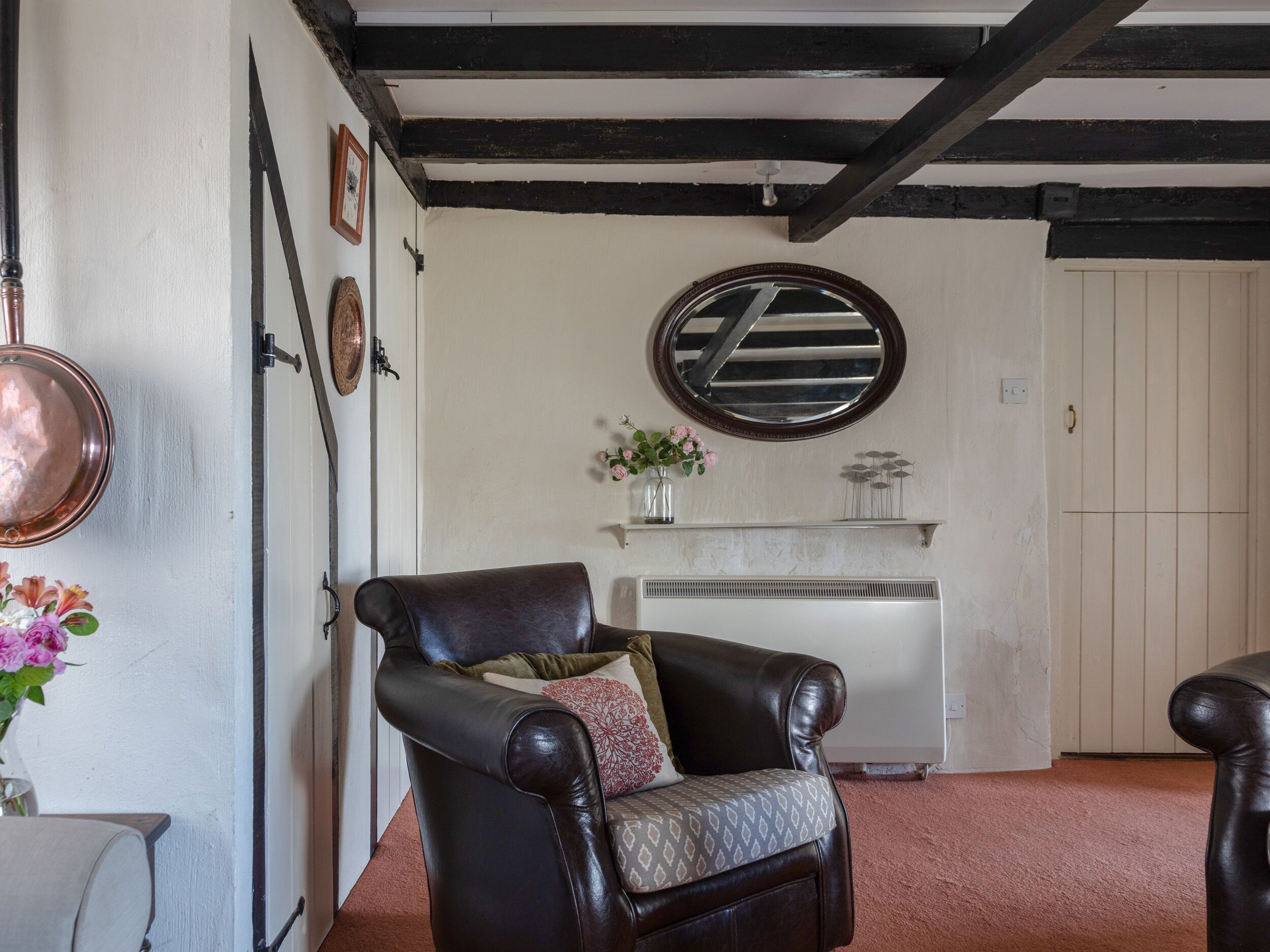 Quarto com poltrona de couro preto, radiador branco, espelho na parede e porta com puxador.
