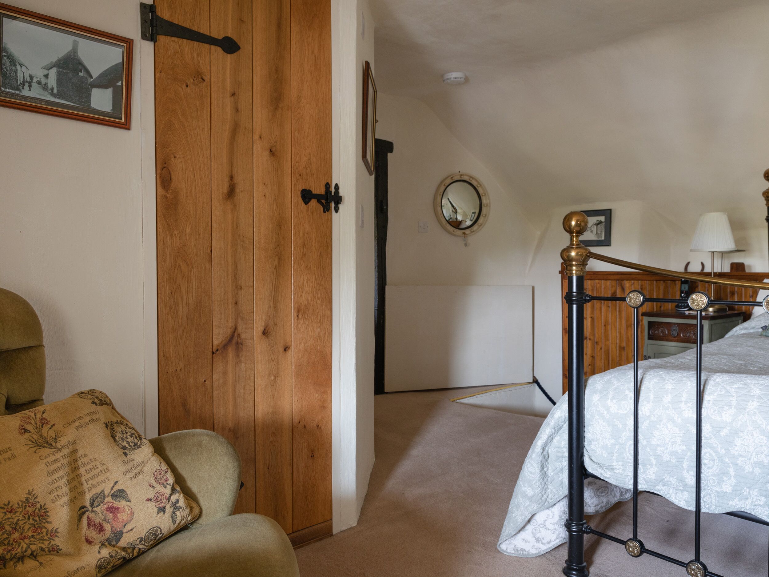 Une chambre avec une porte en bois, un lit avec un cadre en métal, une table de chevet avec une lampe et un miroir fixé au mur.