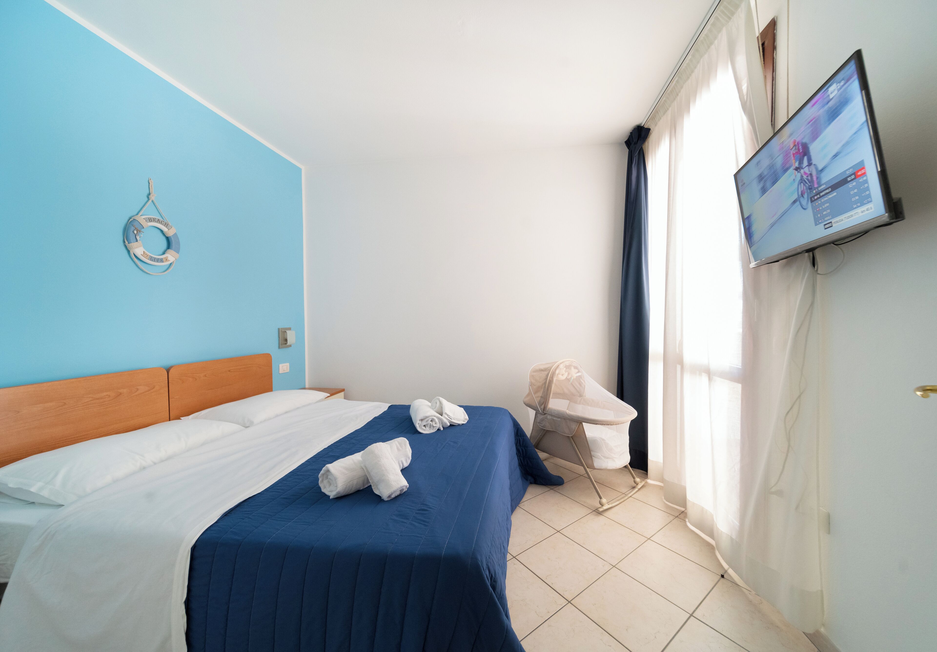 A hotel room with a bed, a television, a chair, and a life preserver on the wall.