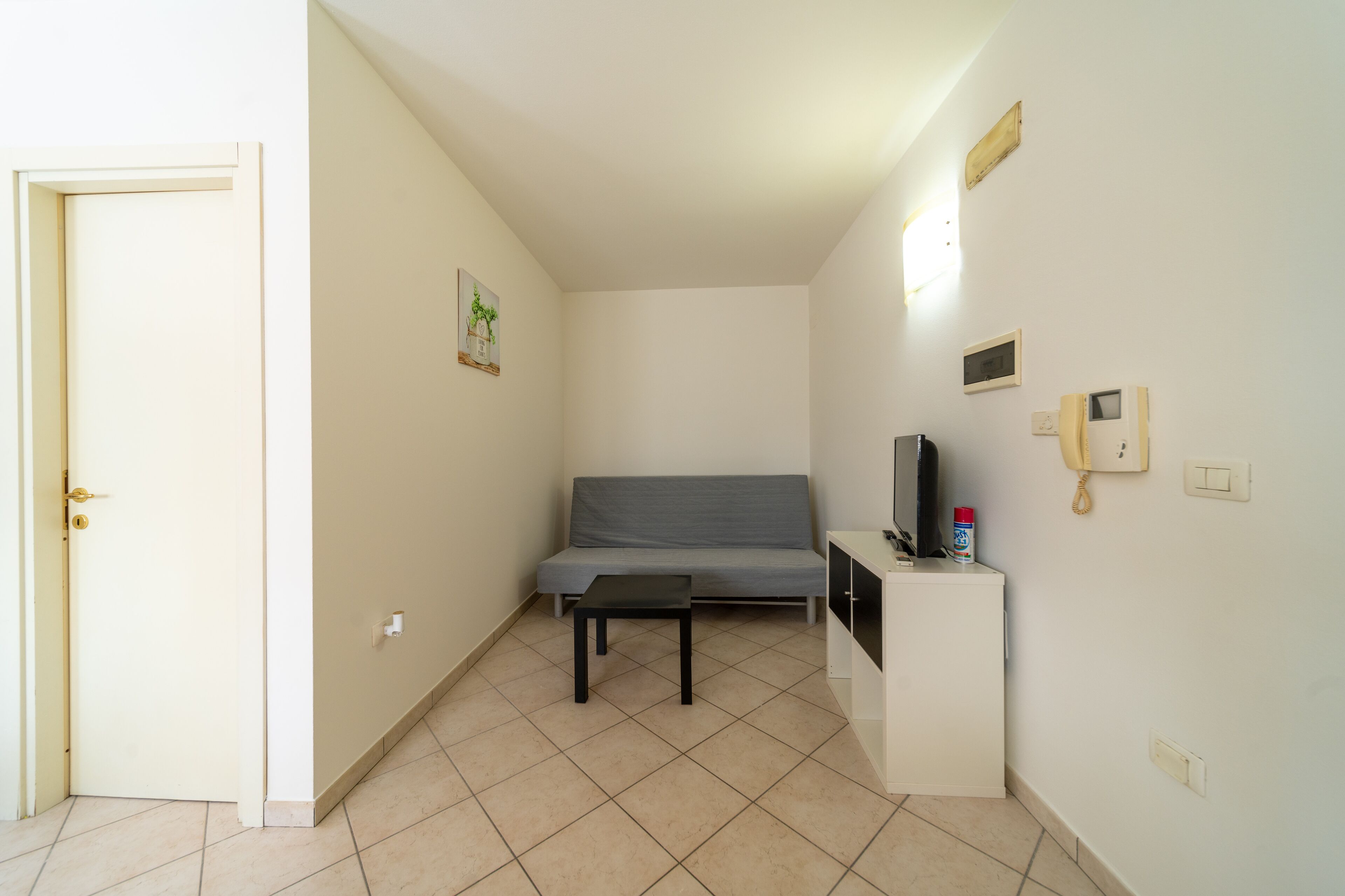A small, clean room with a grey sofa, a small table, a TV, and a phone on a stand.