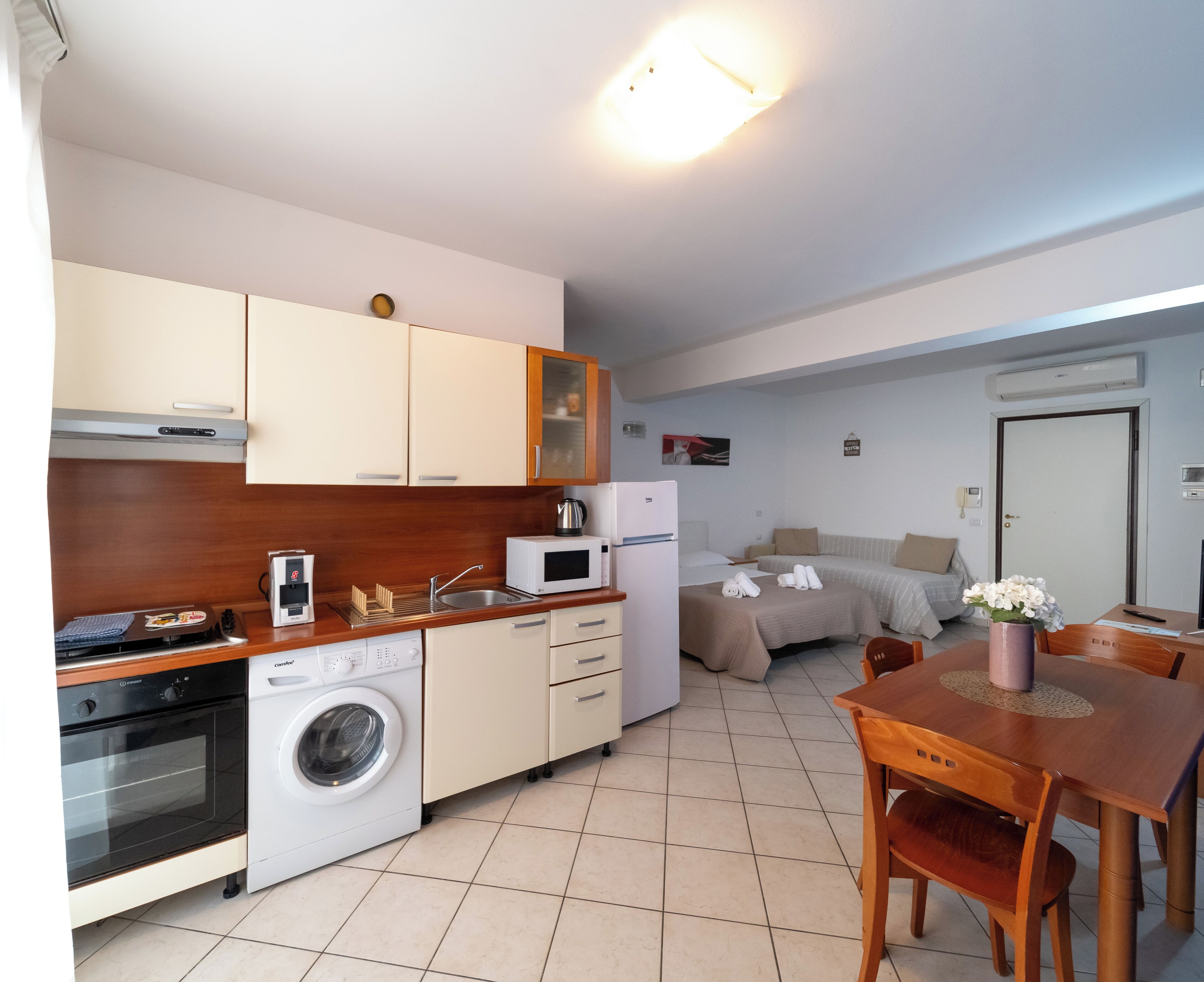 A compact kitchen with a washing machine, microwave, and oven. There is a dining area with a table and chairs.