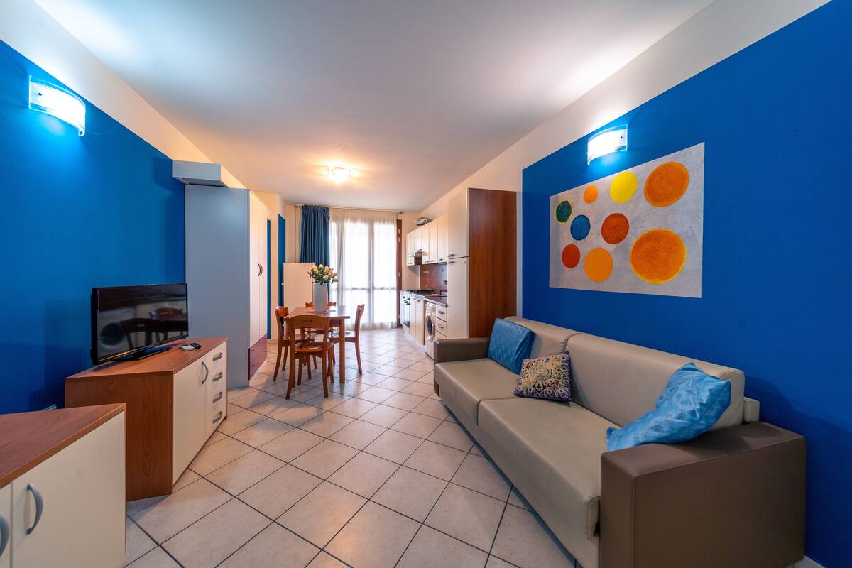 A modern living room with a sofa, a TV, and a dining area with chairs and a table.