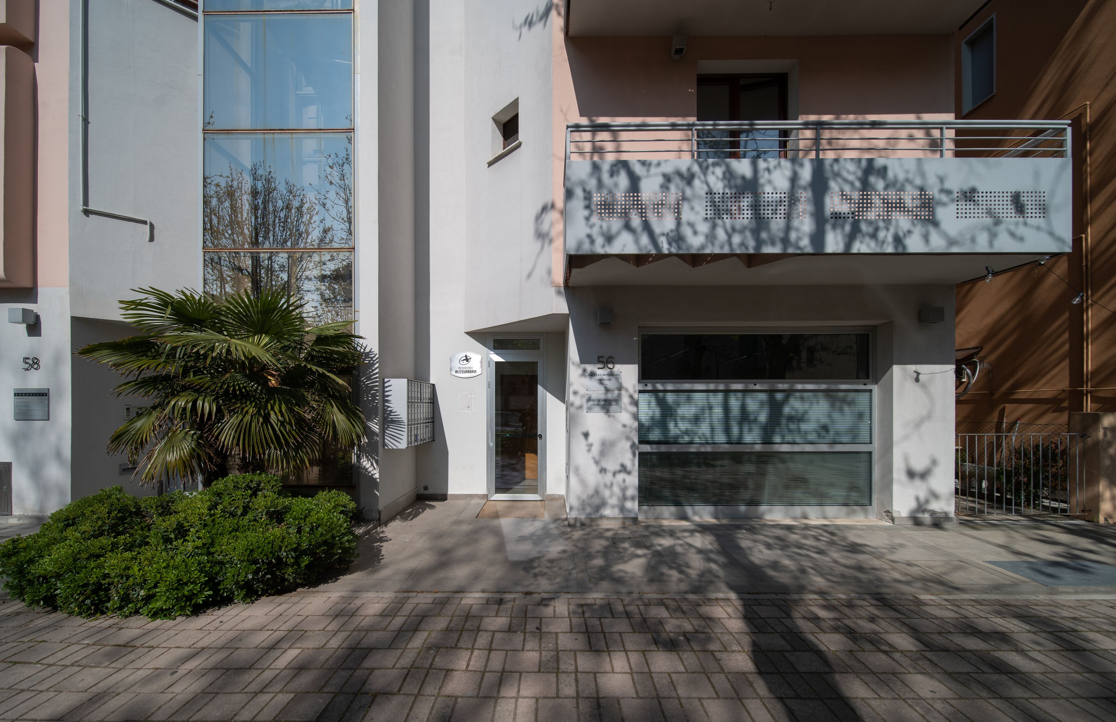 A modern building with a balcony, a palm tree, and a brick-paved entrance.
